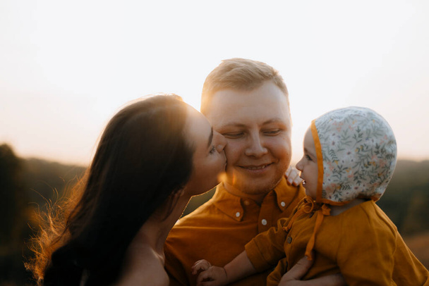 Mutlu bir ailenin portresi. Kadın kocasını yanağından öpüyor. Mutlu baba kızını kollarında tutuyor. Babalar Günü ve Aile Günü - Fotoğraf, Görsel