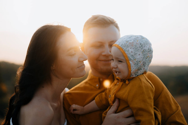 Portret szczęśliwej młodej rodziny z dzieckiem. Kobieta i mężczyzna z dzieckiem o zachodzie słońca. szczęśliwe twarze rodziny oświetlone promieniami słońca. - Zdjęcie, obraz