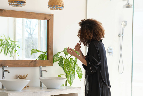 νέα όμορφη γυναίκα ισιώνει τα μαλλιά της στέκεται μπροστά από τον καθρέφτη. πρωινή ρουτίνα έννοια - Φωτογραφία, εικόνα
