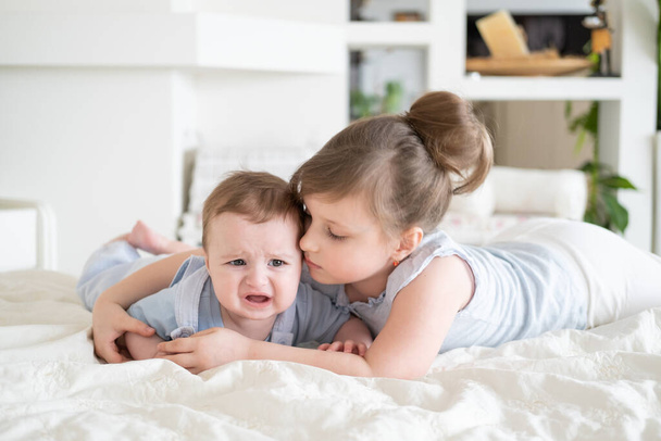 Γλυκό κοριτσάκι μεγαλύτερη αδελφή παρηγορεί κλάμα μωρό αδελφό αγόρι της στο σπίτι - Φωτογραφία, εικόνα