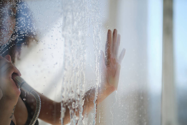mão feminina na porta de vidro do chuveiro. Retrato sensual de uma jovem que toma banho. Desfocado feminino olha através do vidro do chuveiro stall. - Foto, Imagem