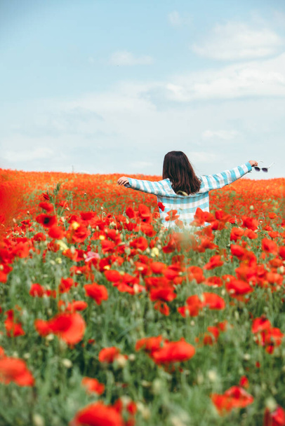 νεαρή όμορφη γυναίκα απολαμβάνει τη ζωή. στέκεται στη μέση του φακέλου με παπαρούνες λουλούδια. οπίσθια όψη. ένα άτομο - Φωτογραφία, εικόνα
