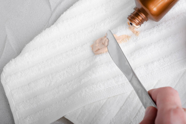 Macchie cosmetiche da vestiti. La mano con un coltello toglie l'autoabbronzante su asciugamani bianchi. Foto di alta qualità - Foto, immagini