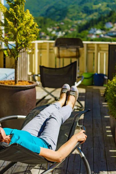 Relax in the sun. Adult woman relaxing resting in deck chair outdoor on veranda. Holiday cottage. - Photo, Image