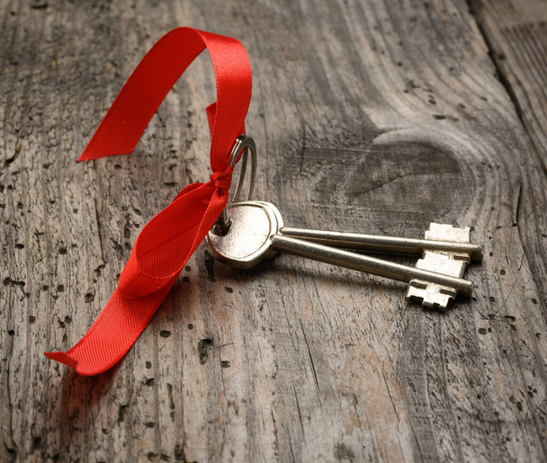 deux clés de porte de maison en métal avec ruban rouge sur fond de bois, concept d'achat immobilier - Photo, image