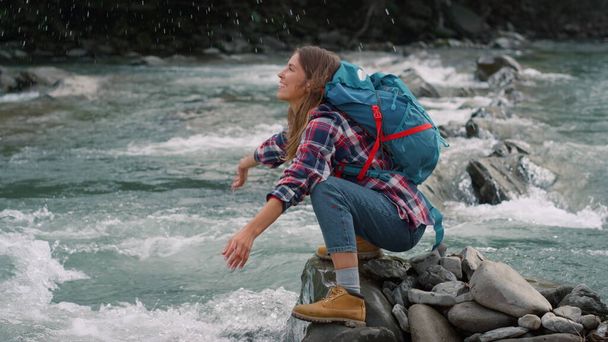 Женщина сидит на берегу реки. Женский турист брызгает водой из ручья - Фото, изображение