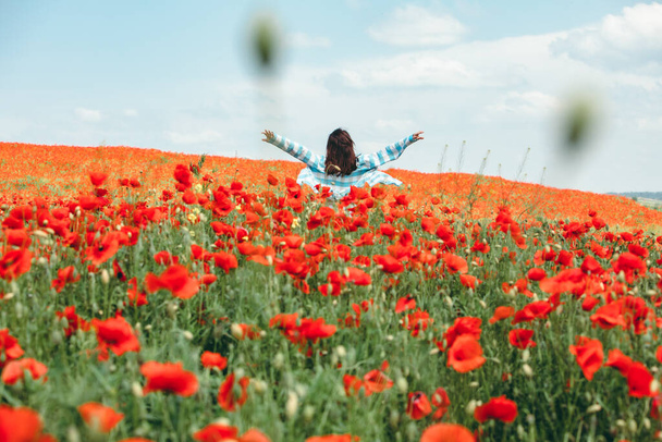 joven bonita mujer disfrutando de la vida. de pie en medio de la limadura con flores de amapola. Vista trasera. una persona - Foto, imagen
