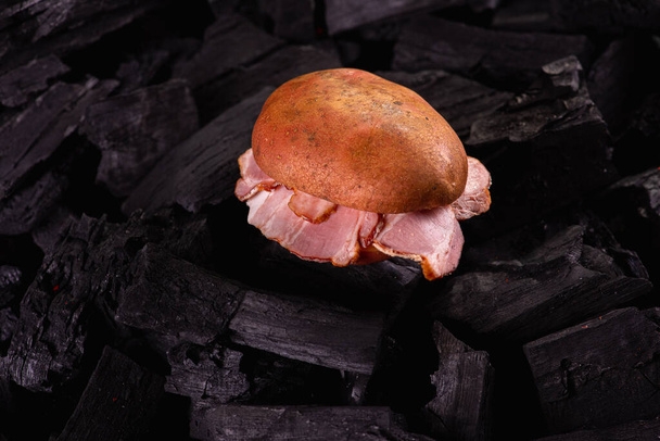 patatas con manteca de cerdo sobre fondo oscuro, sobre carbones. Asando patatas en la parrilla. Bajo perfil. Enfoque selectivo - Foto, imagen