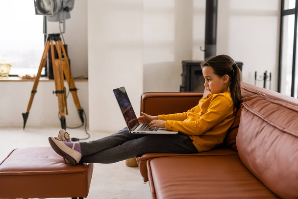 Criança online. Uma menina usa um bate-papo de vídeo laptop para se comunicar aprendendo enquanto está sentado em um laptop em casa - Foto, Imagem