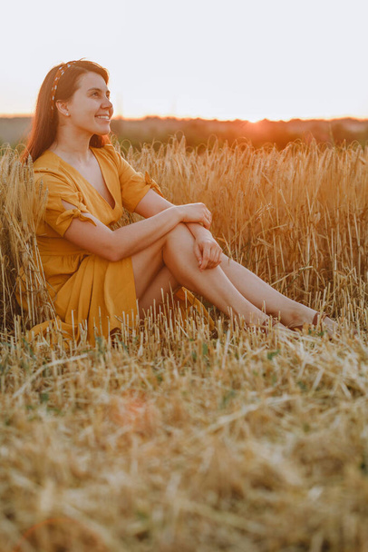 jonge mooie vrouw in gele zonnejurk in het veld bij zonsondergang. poserende portretten - Foto, afbeelding