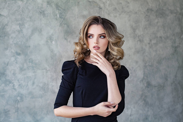 Glamorous woman with curly hair and makeup thinking on gray background portrait - 写真・画像