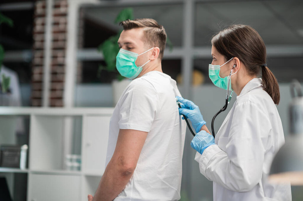 Eine Ärztin in der Klinik führt die Auskultation der Lungen einer Patientin mit Symptomen des Coronavirus durch - Foto, Bild