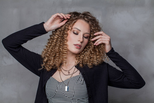 Νεαρή ελκυστική γυναίκα με καστανά σγουρά μαλλιά σε γκρι φόντο πορτρέτο - Φωτογραφία, εικόνα
