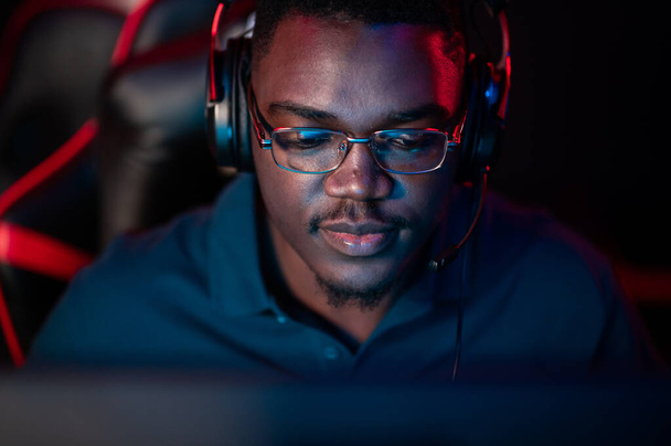 Um retrato de close-up de um homem bonito de pele escura usando óculos e um fone de ouvido na frente de um computador - Foto, Imagem