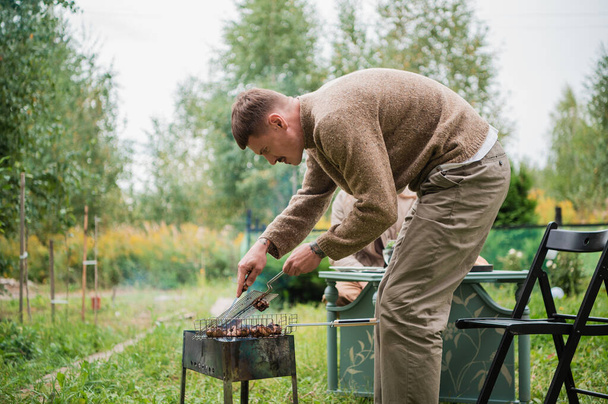Egy fiatal kelet-európai férfi barbecue-t készít, illatos húst süt a grillen. Egy romantikus piknik koncepciója egy fiatal pár számára. - Fotó, kép