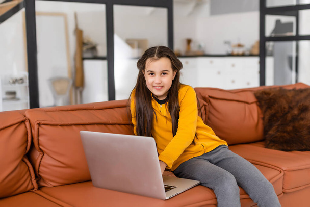 Smart Little Girl macht Hausaufgaben in ihrem Wohnzimmer. Schuppen sitzen und Laptop nutzen. - Foto, Bild
