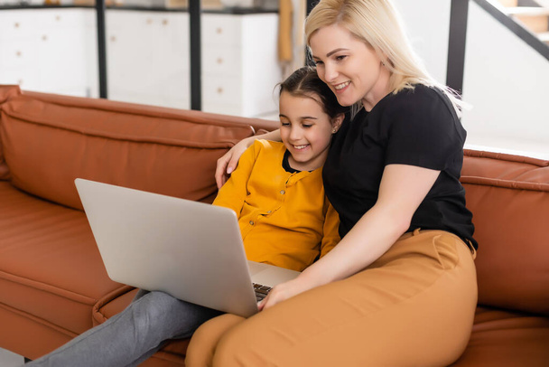 Working from home office with kid. Happy mother and daughter shopping online, using laptop together. Woman hugging child. Freelancer workplace. Female business, virtual communication. - Photo, Image