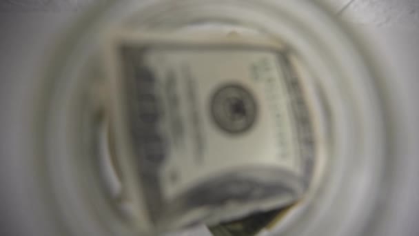 mão colocando uma nota de dólar em um pote de poupança com uma etiqueta branca - Filmagem, Vídeo