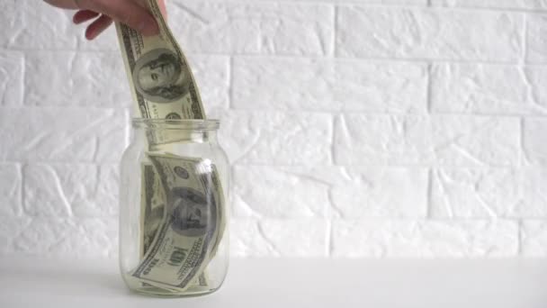 kéz tesz egy dollár számlát egy megtakarítási üveg fehér címkével - Felvétel, videó