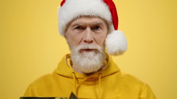 Gelukkige oudere man die binnen cadeautjes geeft. Oude man in santa hoed poseren in de studio - Video