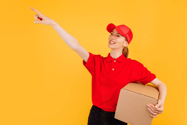 Delivery in red uniform holding a carton box parcel, Female employee working as a courier, on a yellow background, Service concept - Photo, Image