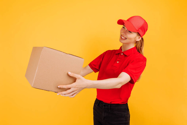 Delivery in red uniform holding a carton box parcel, Female employee working as a courier, on a yellow background, Service concept - Fotografie, Obrázek