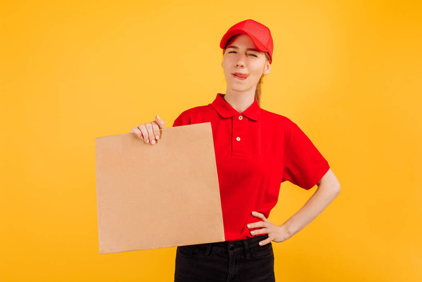 Delivery service employee in a red cap and t-shirt, holding a paper bag with food on an isolated yellow background - Foto, afbeelding