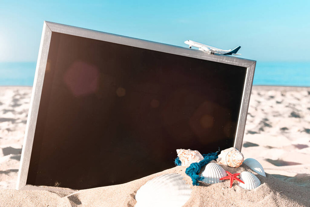 Nyáron. Globe, kagyló, repülőgép és tengeri csillag közelében fekete íróasztal a tengerparton a napsütéses napon. Egzotikus trópusi strand fénymásoló hellyel - Fotó, kép
