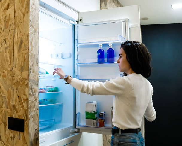 Fiatal nő a hűtő előtt egy üveg vízért. - Fotó, kép