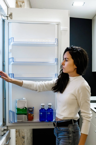 Young woman in front of the fridge gettiing a bottle of water - Фото, зображення