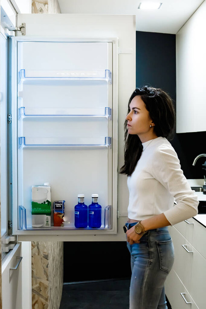 Fiatal nő a hűtő előtt egy üveg vízért. - Fotó, kép