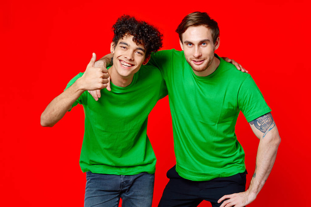 two friends in green t-shirts hugs fun red background - Photo, image