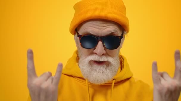 Joyful elderly man posing in studio. Cheerful guy showing rock gesture indoors. - Footage, Video
