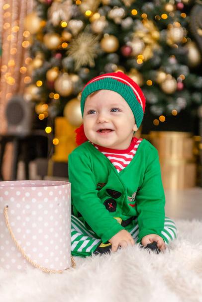 Słodki chłopiec przebrany za elfa otwiera prezent świąteczny w ozdobionym domu Bożego Narodzenia. - Zdjęcie, obraz
