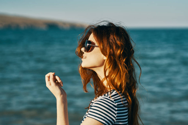 portrait d'une femme rousse en lunettes de soleil dans les montagnes près de la mer et sourire en riant tourisme de voyage - Photo, image
