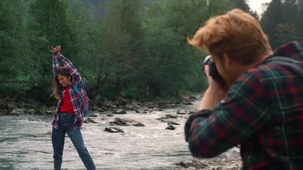 Fotoğraf makinesi olan bir adam kızı vuruyor. Nehir kıyısında kameraya poz veren kadın - Video, Çekim