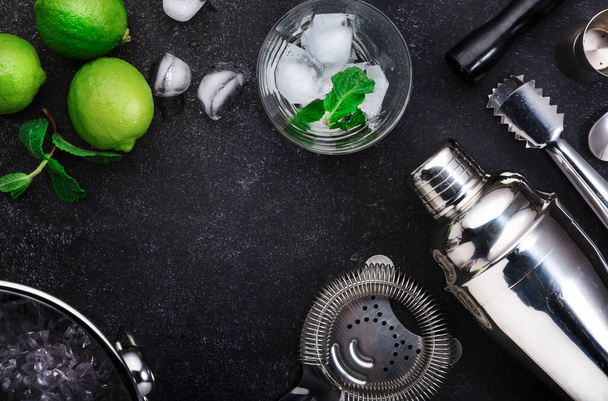Bar tools. Ingredients for mojito cocktail with lime, mint leaves, ice. Cold drink and beverages preparation. Black table, top view with copy space - Photo, Image