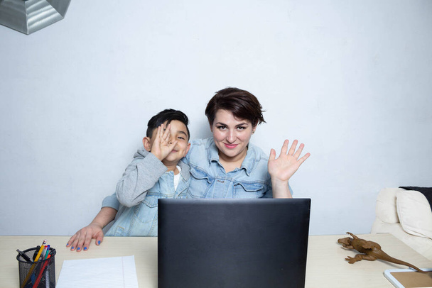 Молодые мама и сын на видео-вызове перед ноутбуком, машут на камеру. Латинская семья - Фото, изображение