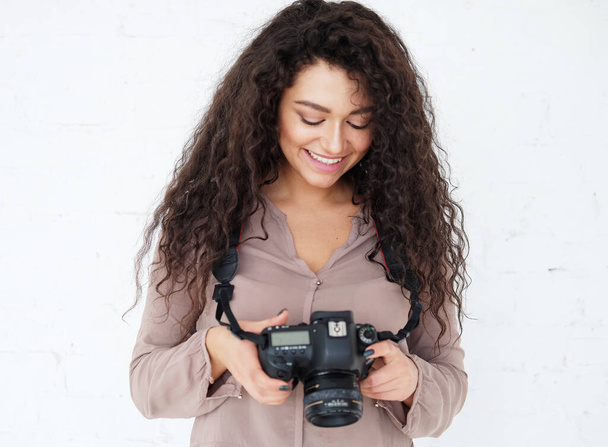 Portrait of Afican woman holding digital photocamera and laughing over white background in studio. - 写真・画像