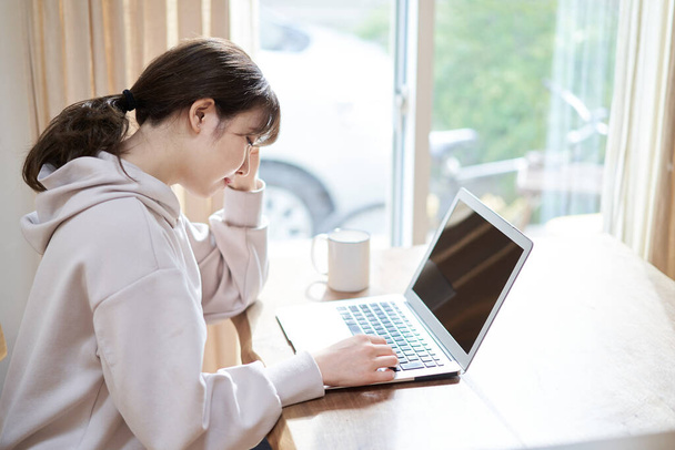 Aasialainen nainen pitelee päätään työskennellessään tietokoneella olohuoneessa - Valokuva, kuva