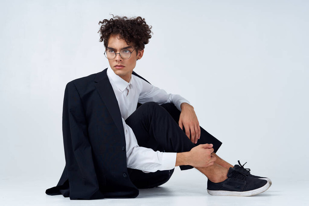 stílusos férfi göndör haj tornacipőben egy könnyű háttér egy kabát a váll nadrág modell - Fotó, kép