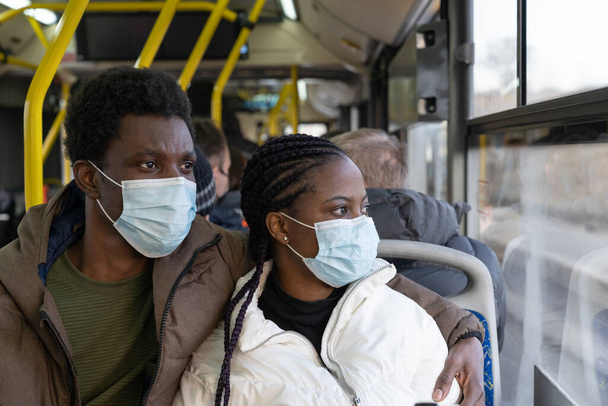 Ζευγάρι σε λεωφορείο φορώντας μάσκες ενώ ταξιδεύουν σε νέα φυσιολογικά. Αφρικανός άνδρας και γυναίκα στα μέσα μαζικής μεταφοράς - Φωτογραφία, εικόνα