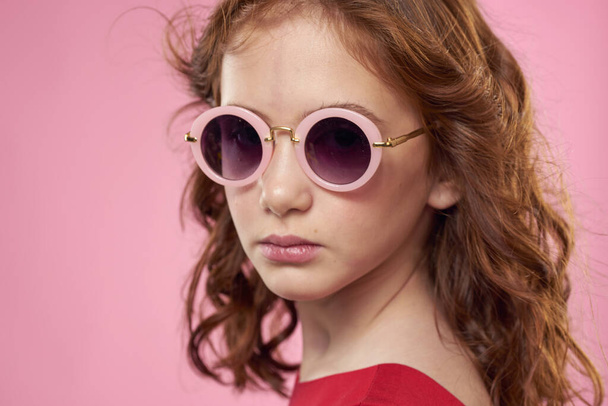 κορίτσι με σγουρά μαλλιά γυαλιά ηλίου παιδική χαρά ροζ φόντο - Φωτογραφία, εικόνα