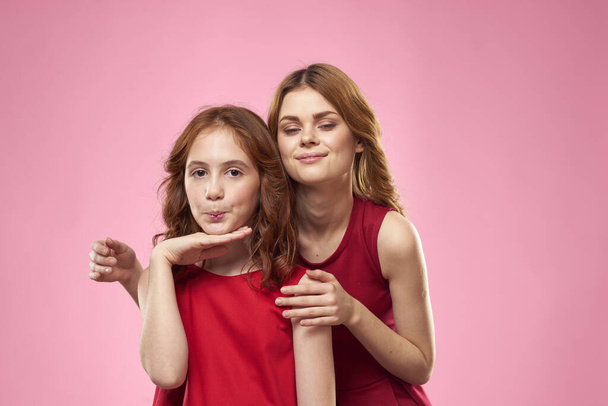 Cheerful mom and daughter wearing red dresses are standing next to joy family on pink background - Fotografie, Obrázek