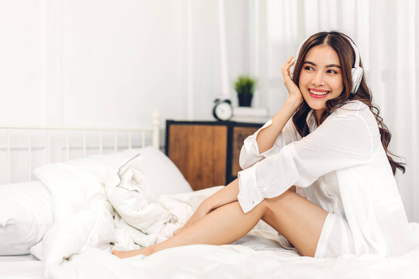 笑顔陽気で美しいアジアの女性の肖像はパジャマ白い服に身を包んだ新鮮な健康的な白い肌をきれいにします.女の子はリラックスして自宅でベッドの上で時間をお楽しみください.アジアの美しさ - 写真・画像