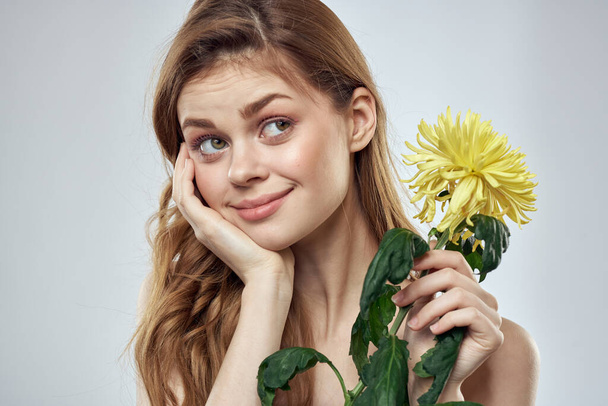 Retrato de una hermosa mujer con una flor amarilla sobre un fondo claro encantadora sonrisa modelo pelo rojo - Foto, imagen