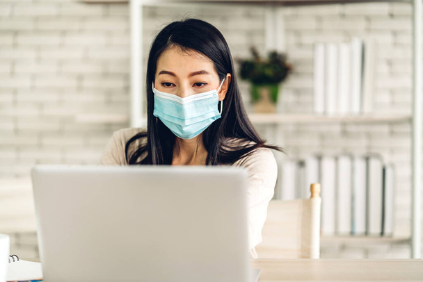 ラップトップコンピュータ作業とビデオ会議を使用して若いアジアの女性は自宅で保護マスクを身に着けているコロナウイルスの隔離のためのオンラインチャット.ホームコンセプトからの仕事 - 写真・画像