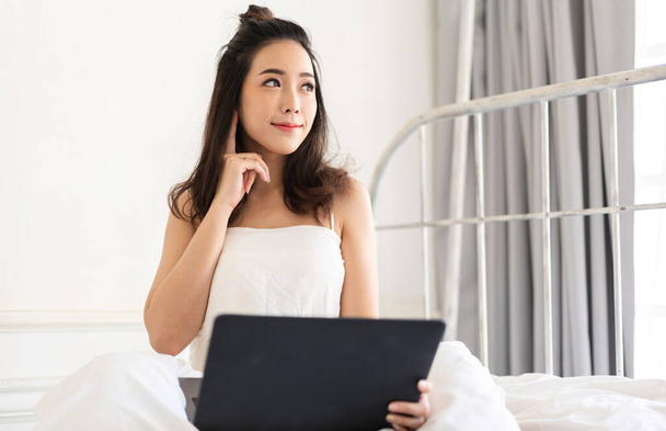 Mladá usměvavá šťastná krásná asijská žena relaxaci pomocí notebooku v ložnici doma. Mladá tvůrčí dívka pracuje a psaní na klávesnici.work z domova koncept - Fotografie, Obrázek