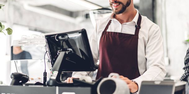 Retrato del hombre barbudo barista guapo dueño de una pequeña empresa que trabaja con el ordenador portátil detrás de la barra de mostrador en un café - Foto, imagen