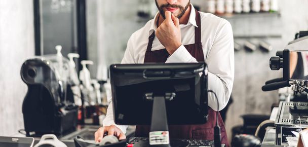 Portret van een knappe barista man met baard, kleine ondernemer, werkend met laptop achter de bar in een café - Foto, afbeelding